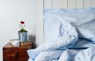 Bedroom in rustic style, pillow and blanket, blue linen, bedside table with a flower, close-up.